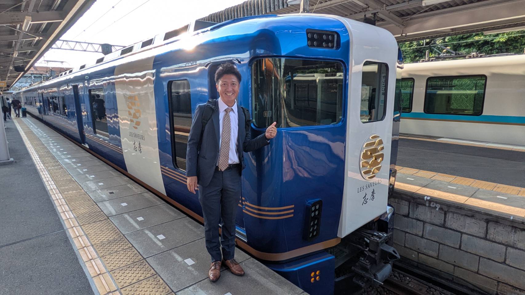 「レ・サヴール・志摩」の車両の前でサムズアップしている男性"